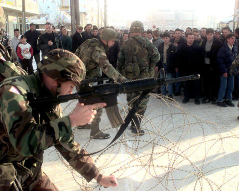 NATO soldiers uncoil two rows of concertina wire to maintain crowd control as residents of Vitina, Kosovo, protest in the streets on Jan. 9, 2000.
